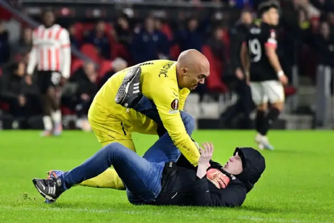 Marko Dmitrovic berusaha menghentikan seorang fan PSV Eindhoven yang menyerbu lapangan di pentas Liga Europa.